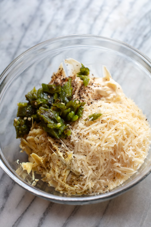 clear bowl filled with chopped jalape&ntilde;os, shredded parmesan, chopped artichokes, mayonnaise, black pepper