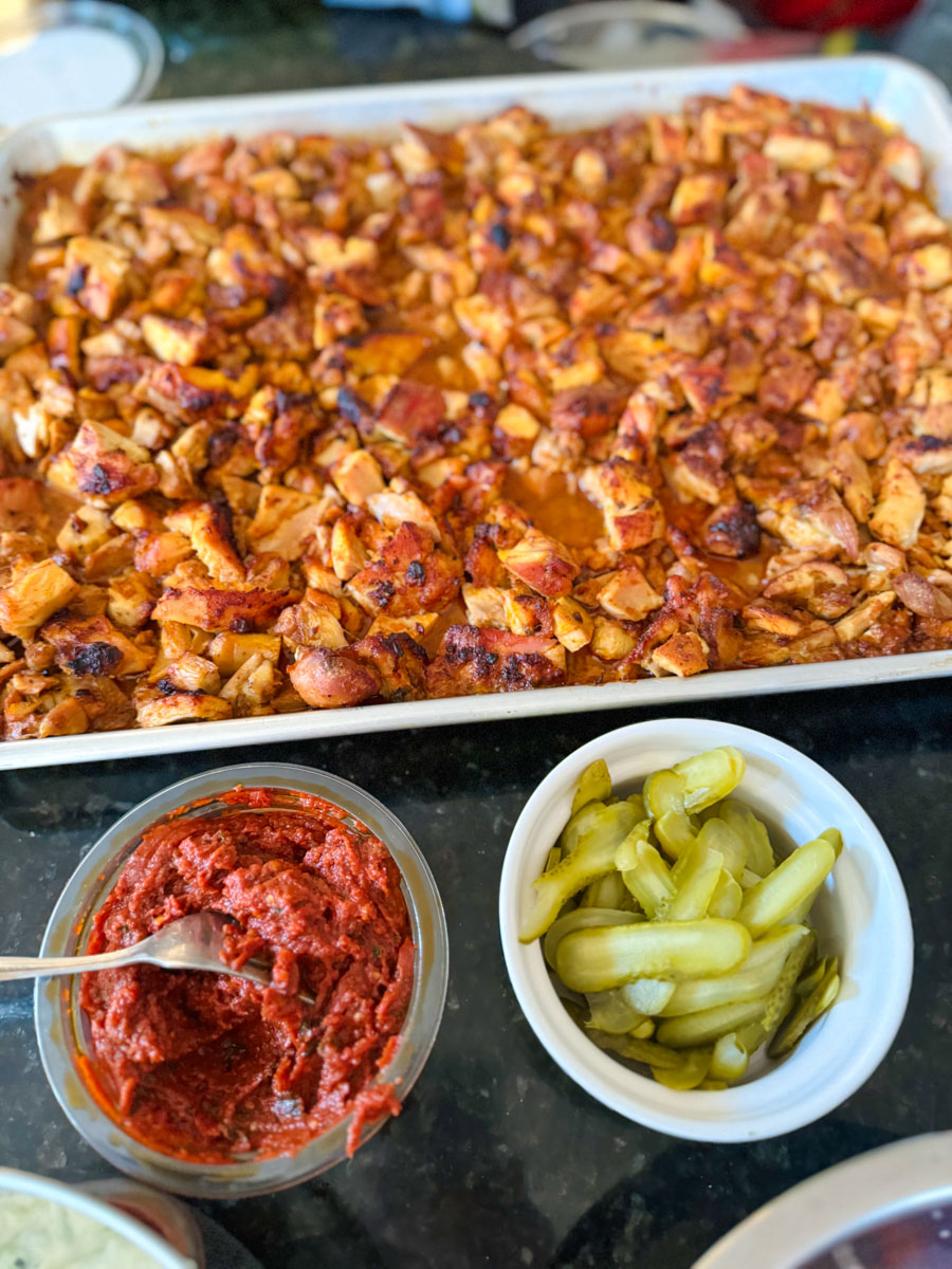 Broiled boneless skinless chicken thighs chopped and charred on a sheet pan with chili paste and sliced pickles.