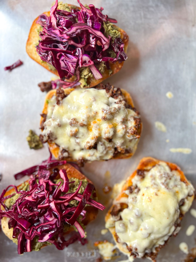 opened faced chorizo sandwiches with melted cheese on half and mashed avocado and cabbage on the other half