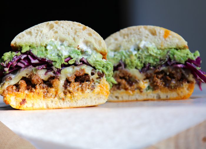 Chorizo Torta cut in half topped with melted cheese, red cabbage, and mashed avocado on parchment paper. 