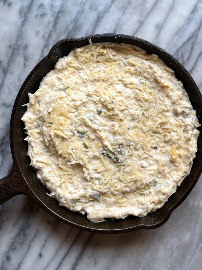 cast iron skillet with uncooked jalape&ntilde;o artichoke dip with shredded parmesan cheese on top 