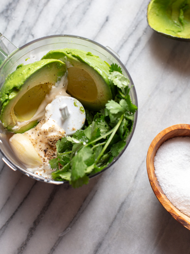 avocado, garlic, cilantro, mayonnaise, in a food processor bowl with a small wood salt bowl on the side
