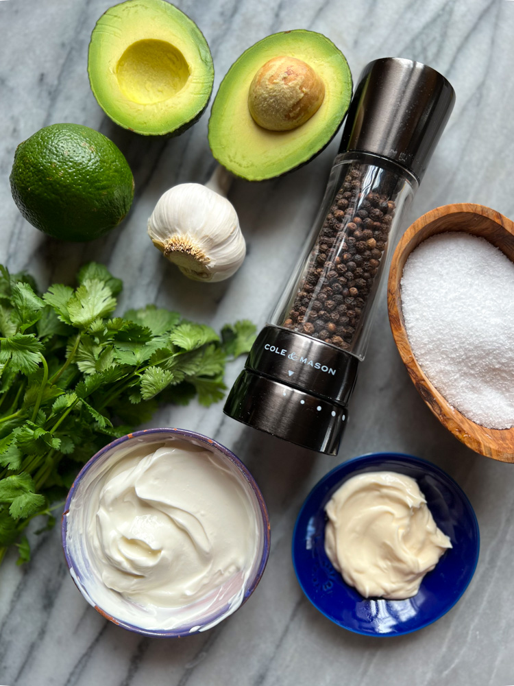 ingredients for avocado cream: cilantro, limes, garlic, pepper grinder, salt, sour cream, mayonnaise, avocado