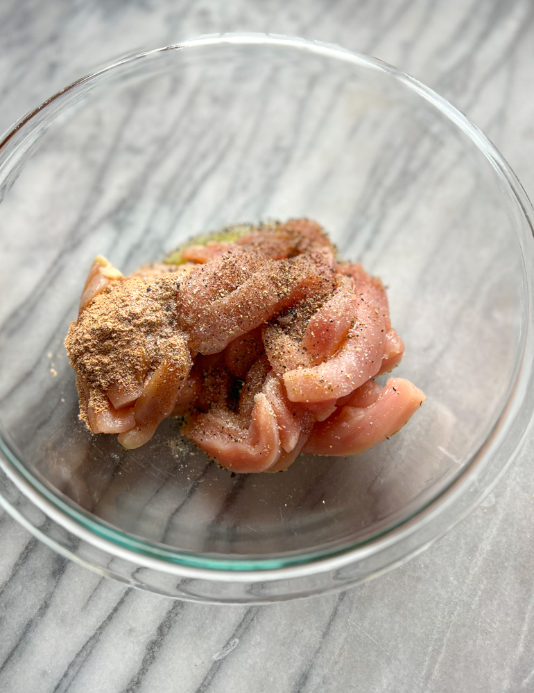 chicken breast slices in a glass bowl with fajita seasoning on top