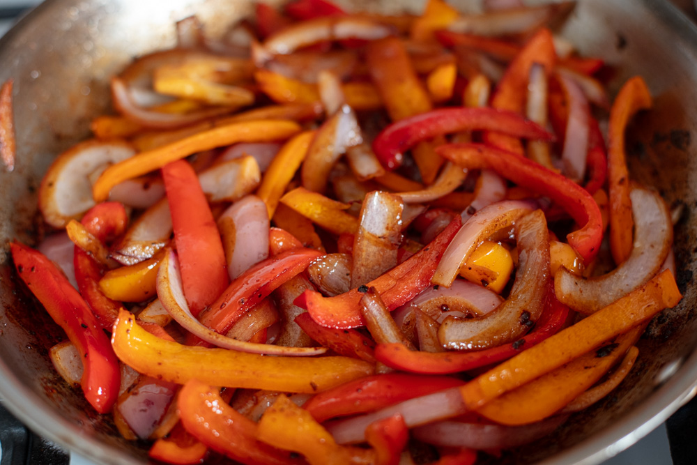 stainless steel skillet with saut&eacute;ed peppers and onions