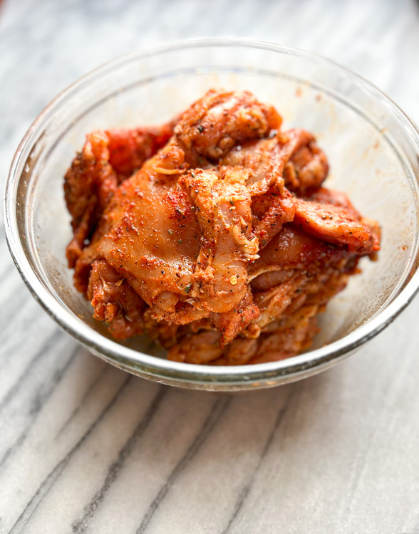 raw chicken thighs with seasoning in glass bowl