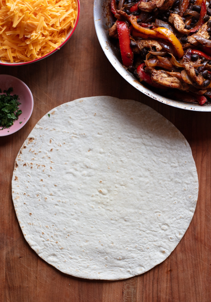 flour tortilla in center of cutting board with fajita fillings around the top