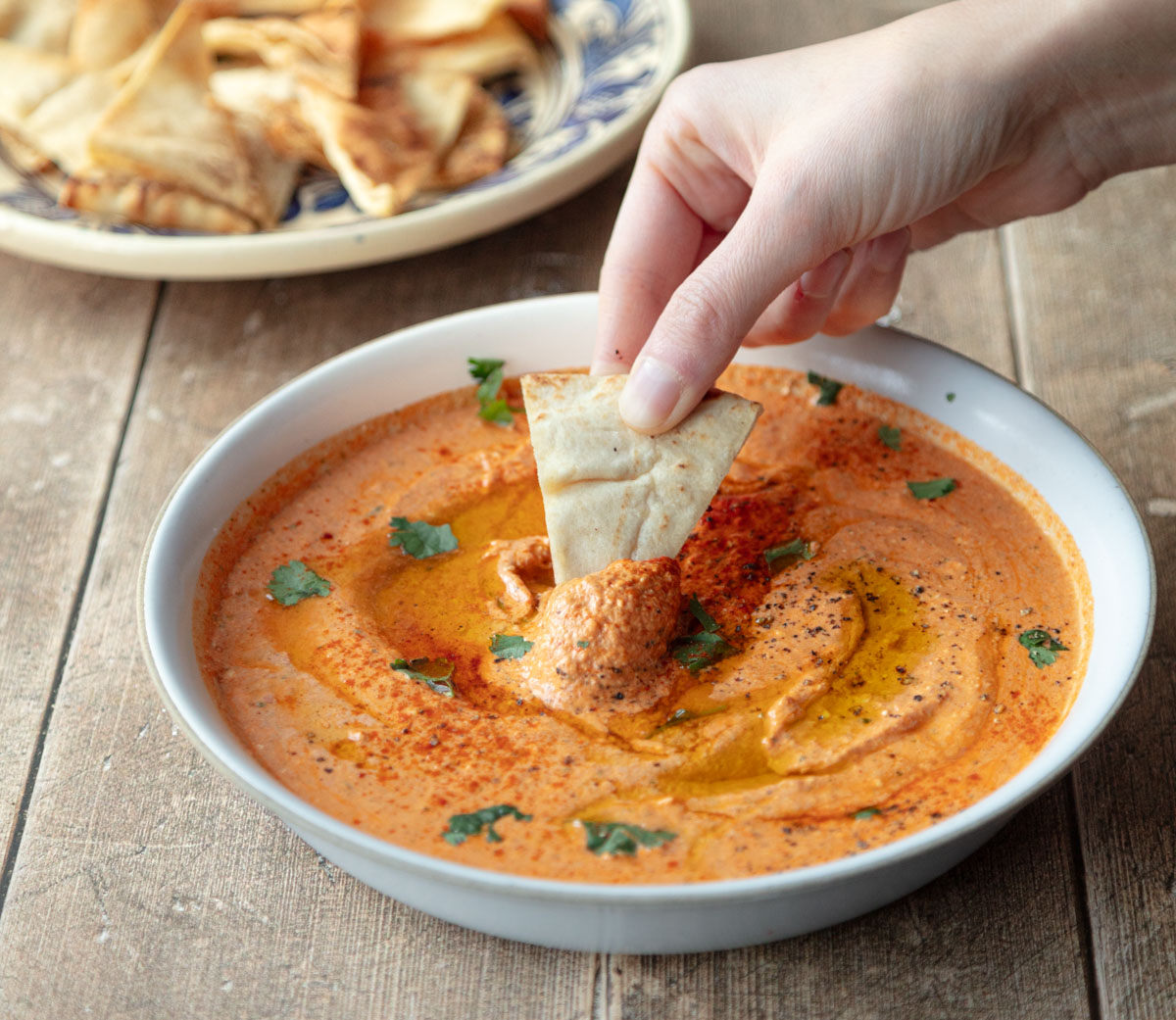 shallow bowl with paprika dip with hand dipping pita chip
