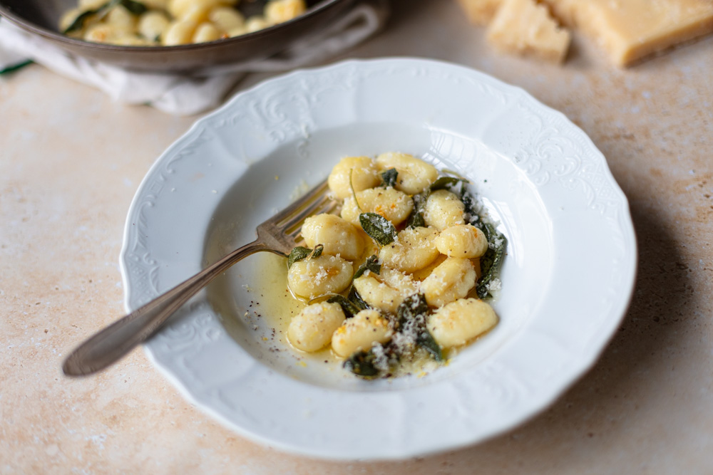 gnocchi with sage butter sauce in shallow bowl with grated parmesan