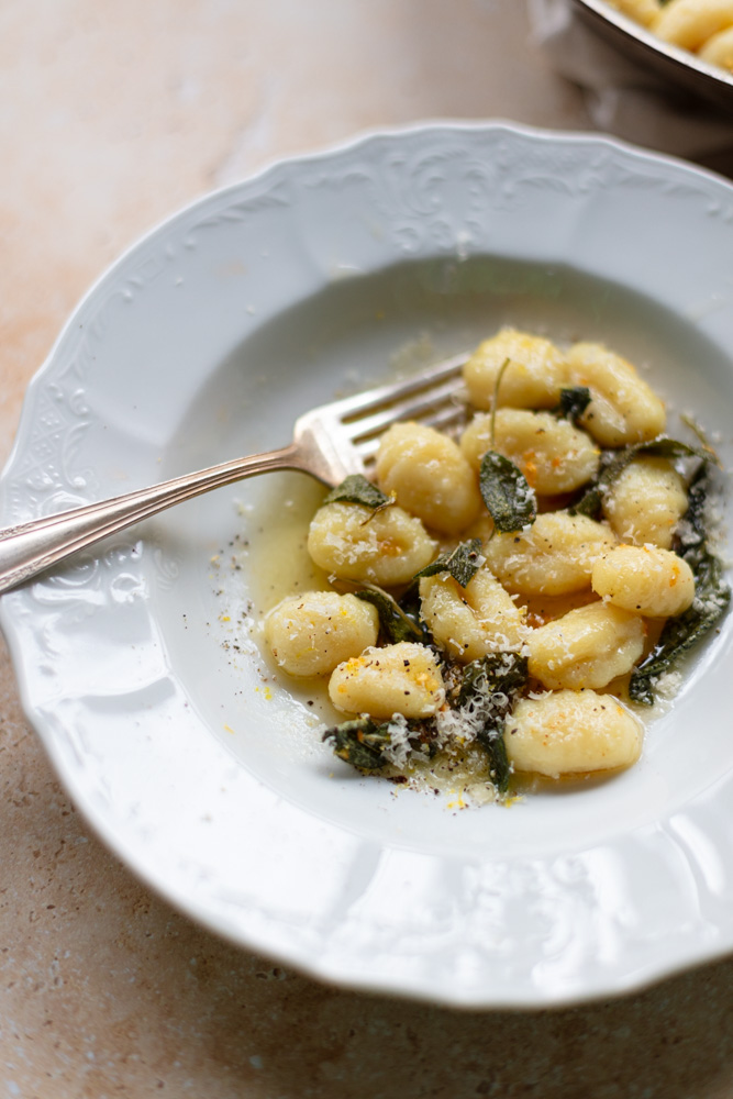 gnocchi and sage butter sauce with grated parmesan cheese in shallow white bowl with fork