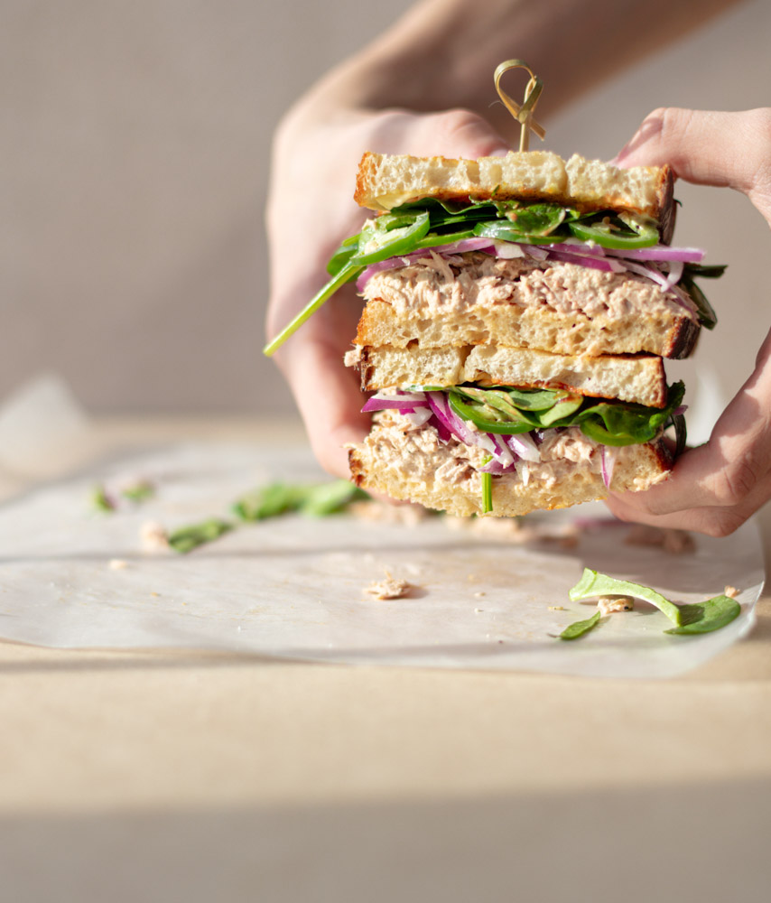 Spicy tuna sandwich made with canned tuna, Sriracha mayo, fresh spinach, and red onion on toasted multigrain bread