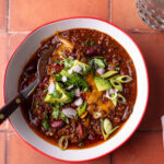 chili bowl with toppings and spoon on tile tabletop