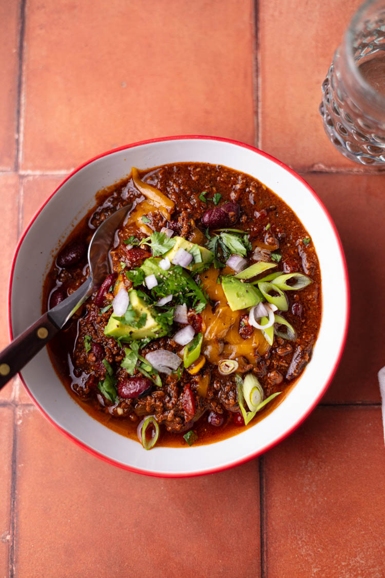 chili bowl with toppings and spoon on tile tabletop