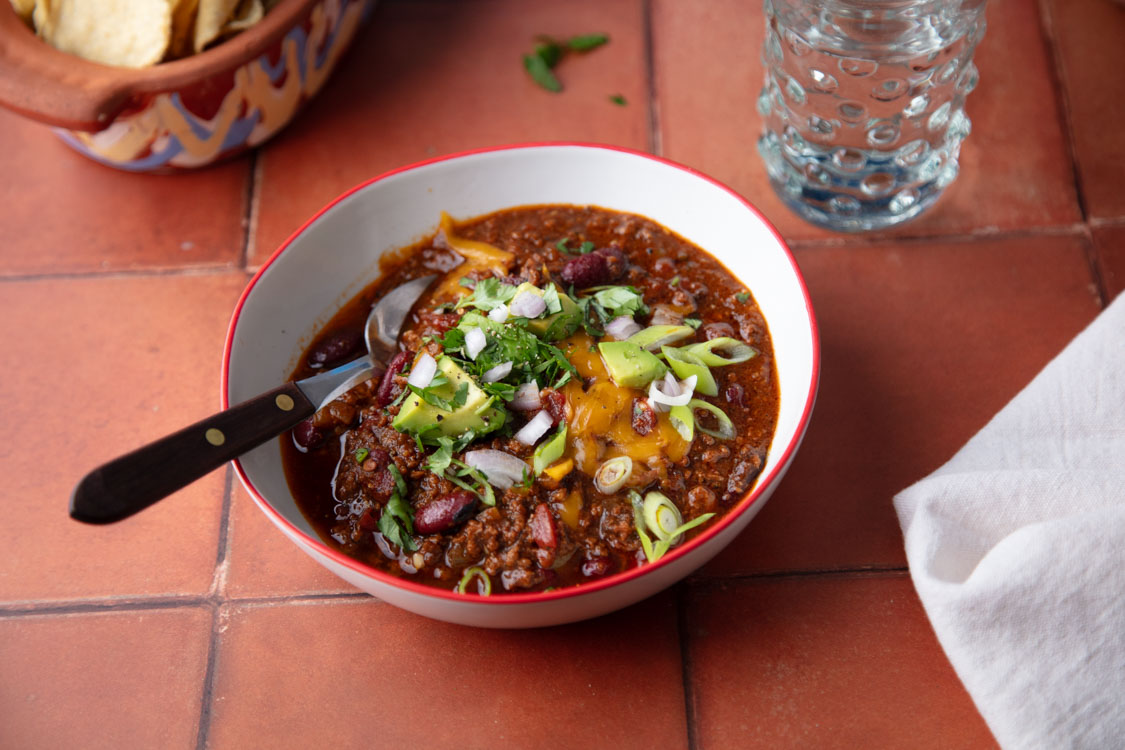 chili bowl with toppings and spoon on tile tabletop