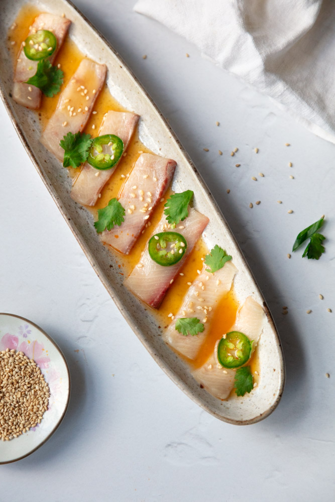 hamachi crudo on narrow dish with sesame seeds in a small bowl