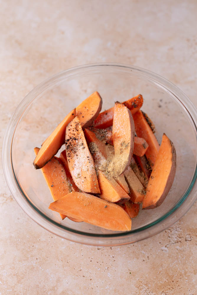 raw sweet potato wedges with dried spices on top in a glass bowl