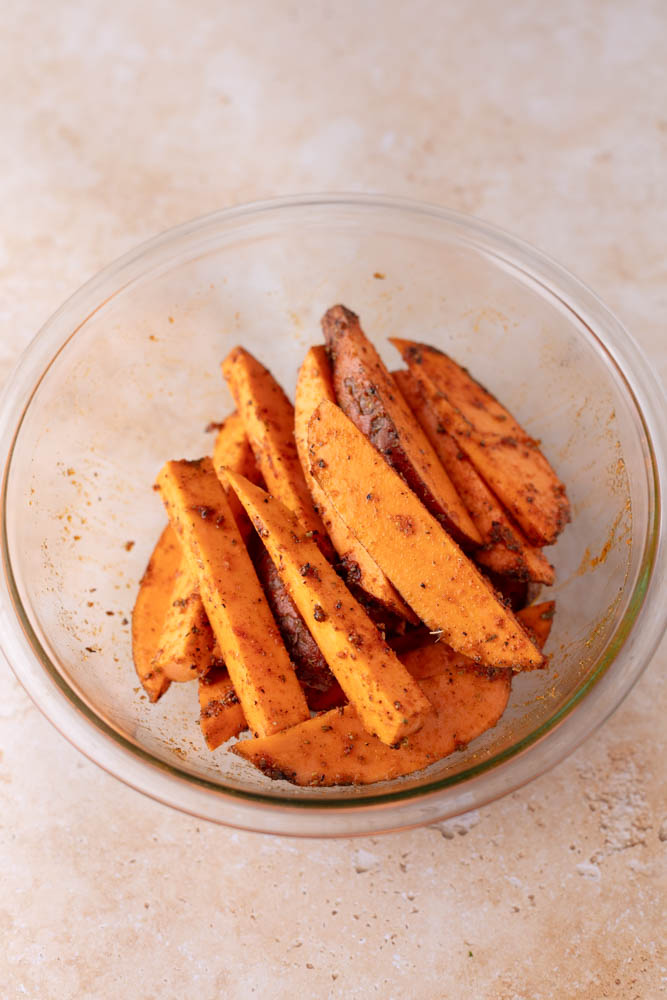 raw sweet potatoe wedges coated in spices in a glass bowl