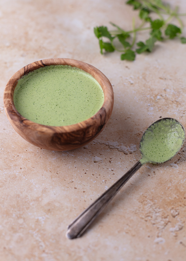small wooden bowl with cilantro jalapeno sauce with a spoon to it