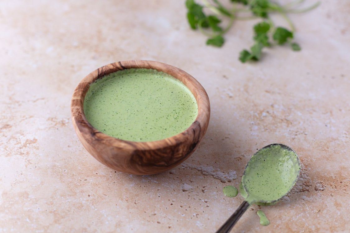 small wooden bowl with cilantro jalapeno sauce with a spoon to it