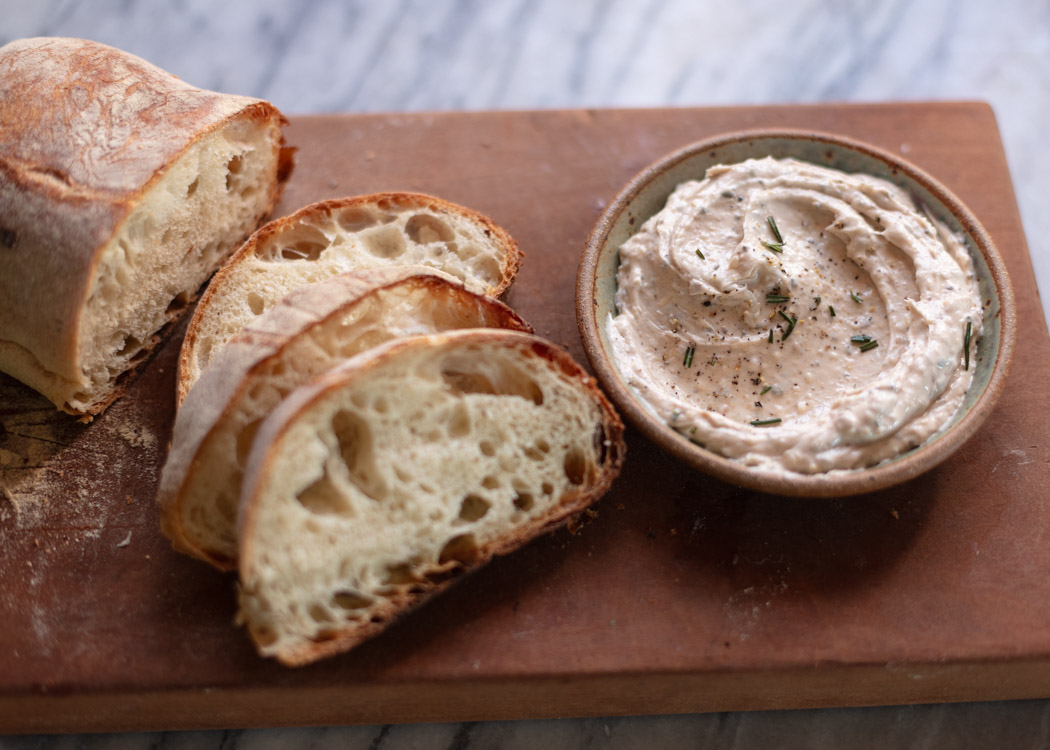 bone marrow butter in small bowl with sliced bread on cutting bread