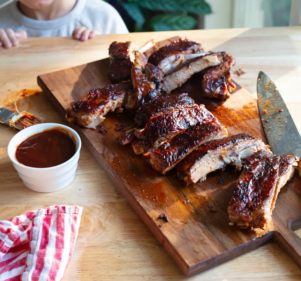 oven baked st. louis ribs cut on a cutting board with sauce on the side