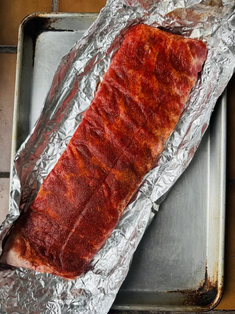 rack of raw st louis style ribs seasoned on foil and a baking sheet