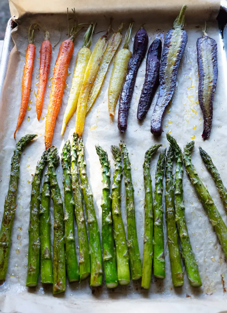 Roasted carrots and asparagus on a sheet pan lined with parchment paper.
