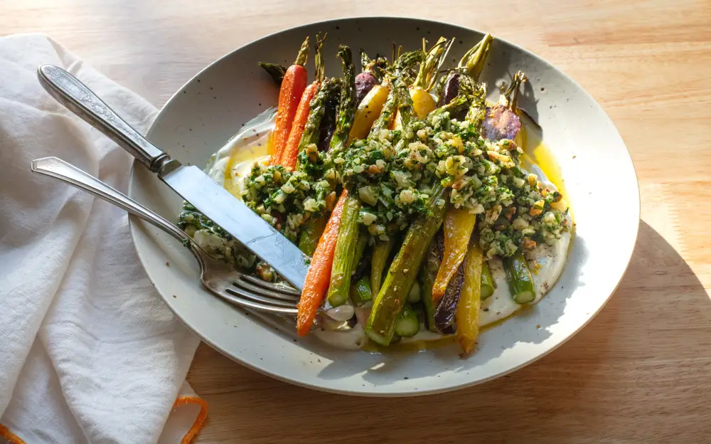 Bowl of roasted veggies and chunky peso in the sunlight on a wooden background.