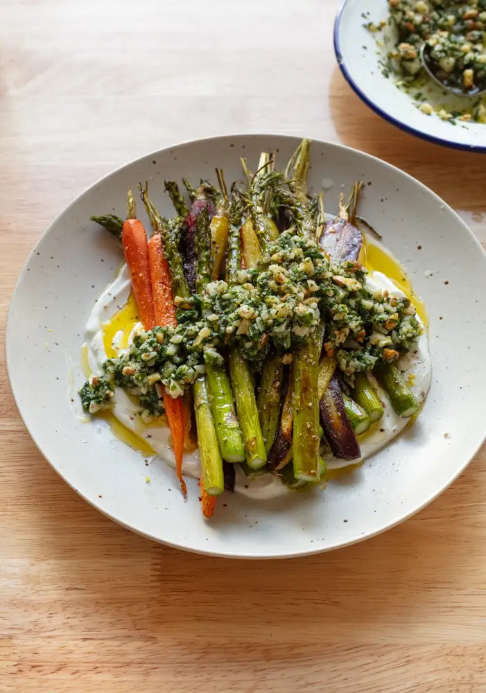 Bowl of roasted asparagus and carrots with chunky pesto on a bed of yogurt.