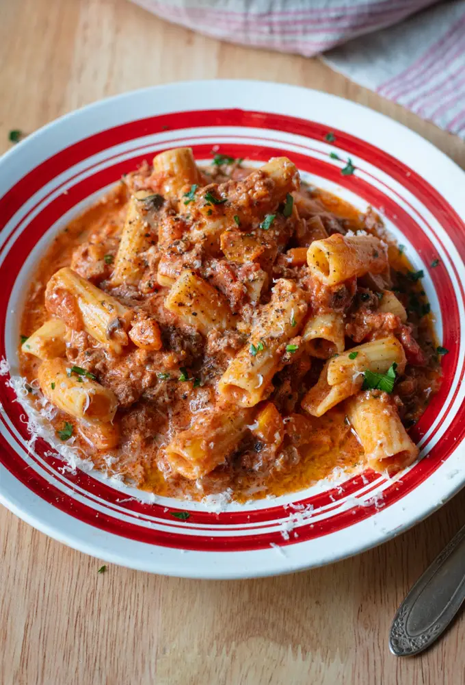 Creamy meat sauce with pasta on a white plate with red trim and napkin on table