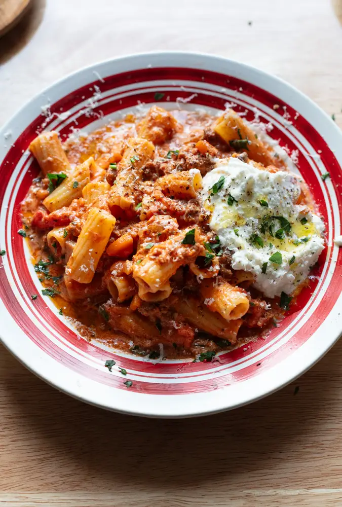 Rigatoni pasta with meat sauce and ricotta dollop on top on a plate