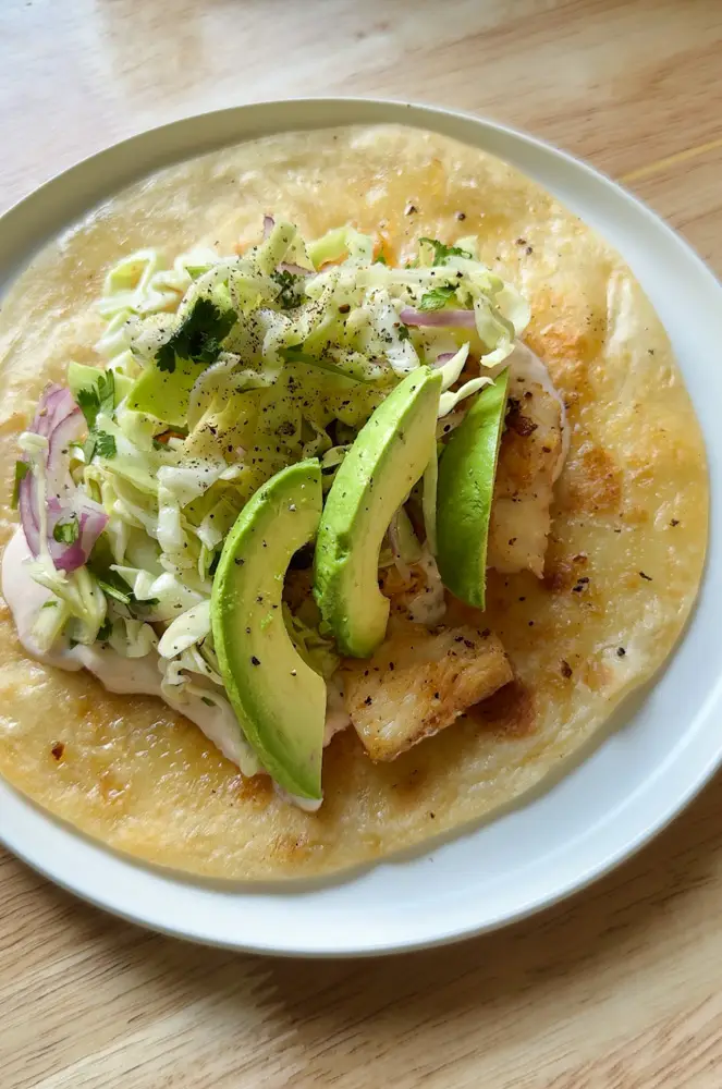 tortilla topped with fish, cabbage, avocado slices