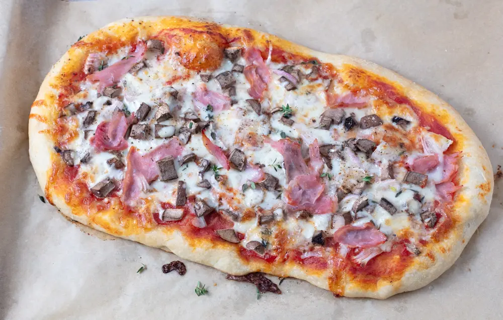 oval pizza with ham and mushrooms on brown parchment paper