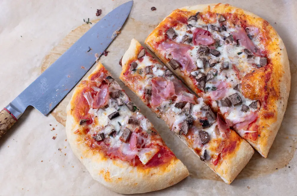 oval ham and mushroom pizza cut in thirds with a knife on parchament paper