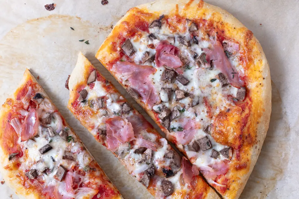 oval pizza with mushroom and ham cut in slices on parchment paper