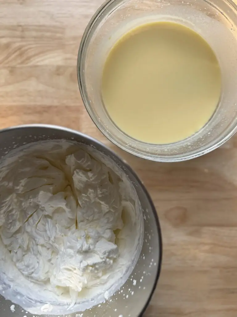 Whipped cream in one mixing bowl next to another mixing bowl of vanilla pudding.