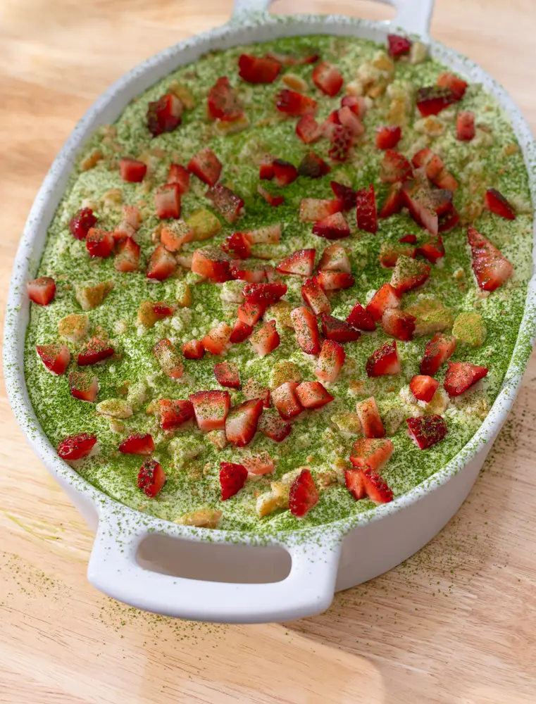 Strawberry banana pudding in a serving dish topped with diced strawberries, bananas and a sprinkle of matcha.