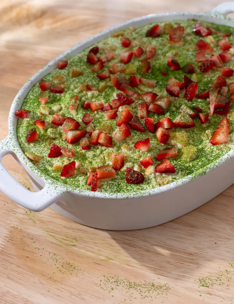Matcha strawberry banana pudding in a serving dish topped with diced strawberries and a sprinkle of matcha.