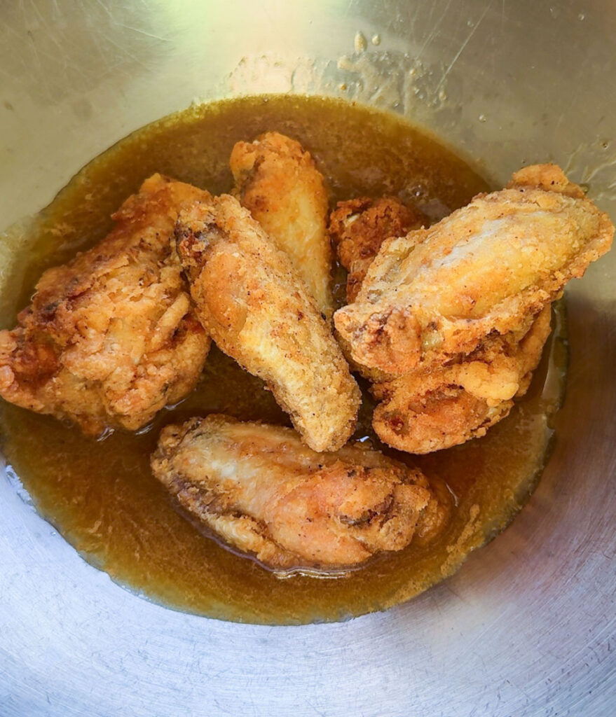 cripsy chicken wings in hot honey sauce in stainless steel bowl