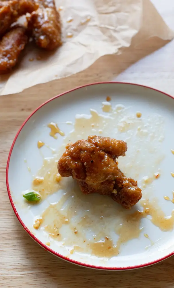 One hot hone wing on a plate with more on a piece of parchment next to it.
