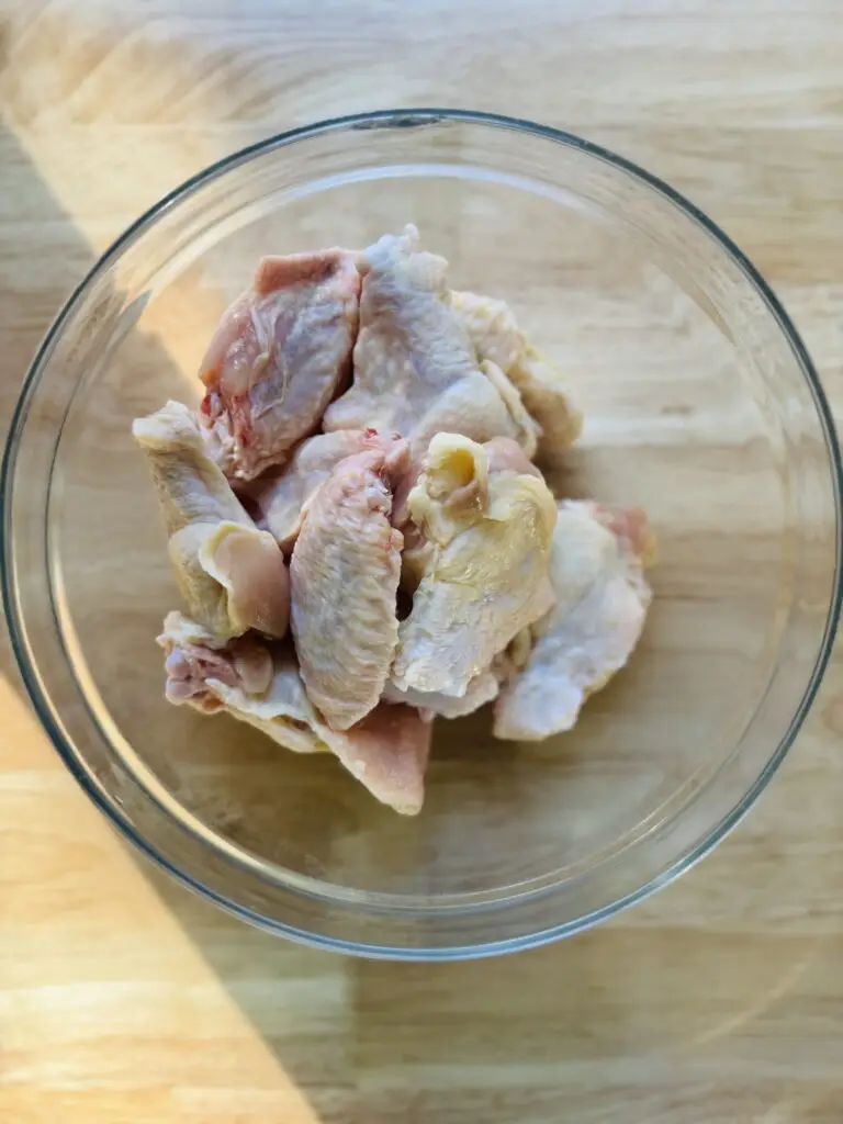 Raw chicken wings in a large glass mixing bowl.
