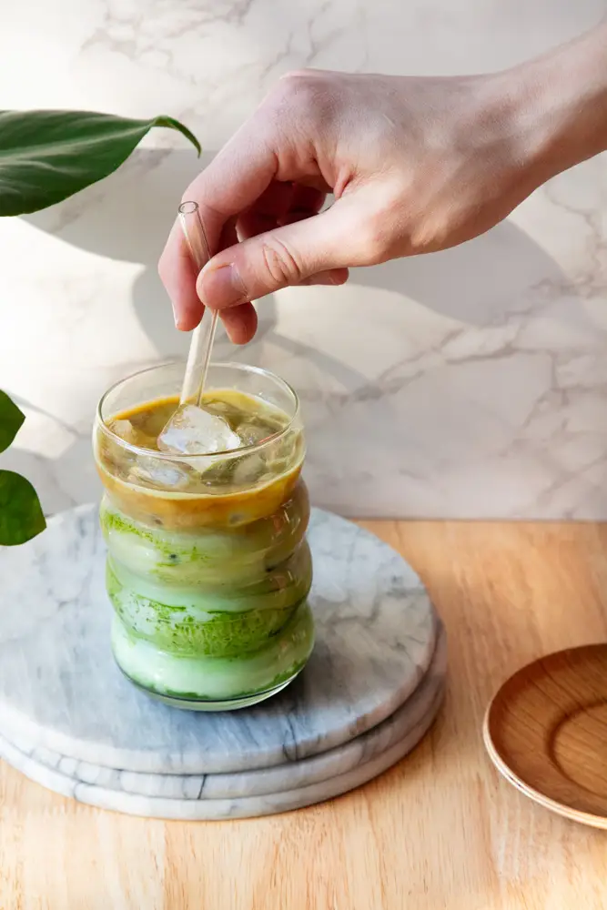 Hand placing a glass straw into the iced dirty matcha latte.