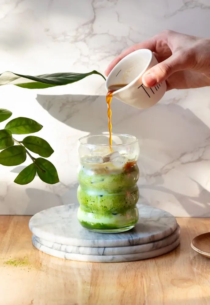 Hand pouring the espresso into the matcha latte.