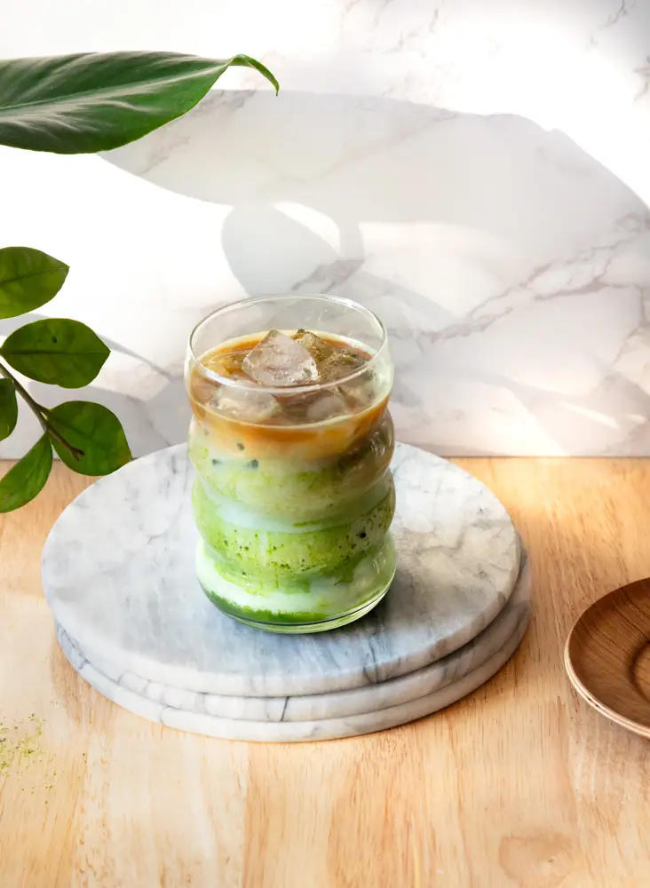 Iced dirty matcha latte in a glass on a stack of marble plates.