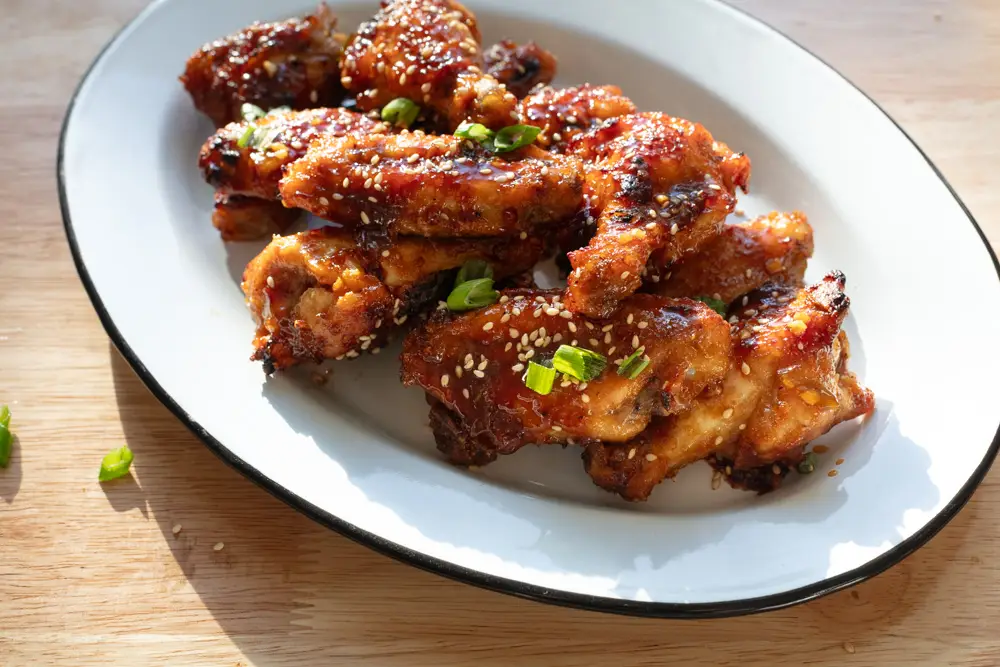 Soy garlic chicken wings on a serving platter topped with sesame seeds and green onions.