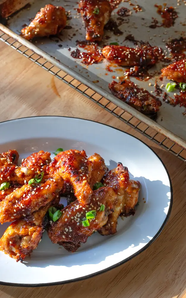 Soy garlic chicken wings on a sheet pan being transferred to a serving platter.
