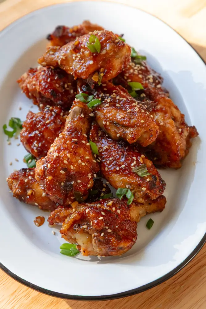 Crispy garlic soy chicken wings served on a serving tray with sesame seeds and green onions on top.