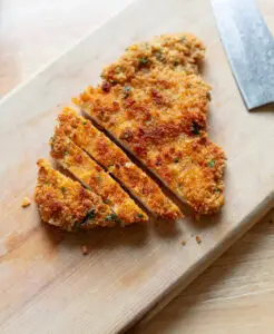Sliced chicken schnitzel on a wooden cutting board.