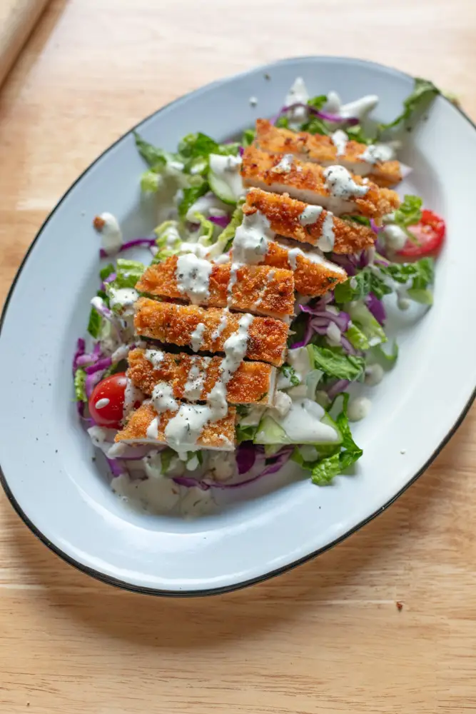 Chicken schnitzel served on top of bed of salad with homemade blue cheese dressing on top.