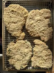 Four breaded chicken fillets on a wire wrack before cooking.